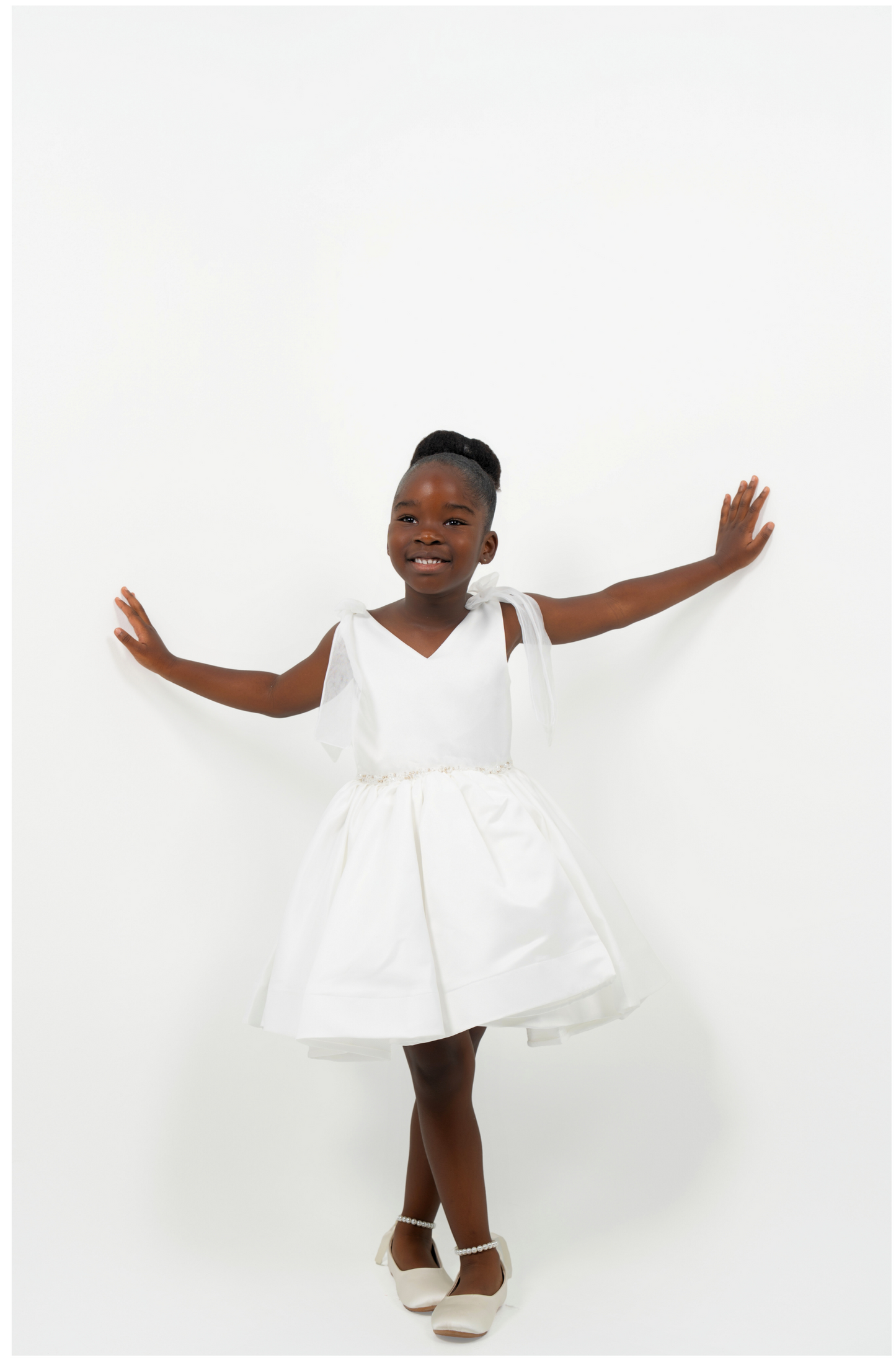 Girl wearing white satin dress with bow straps and full skirt, perfect for flower girl or birthday