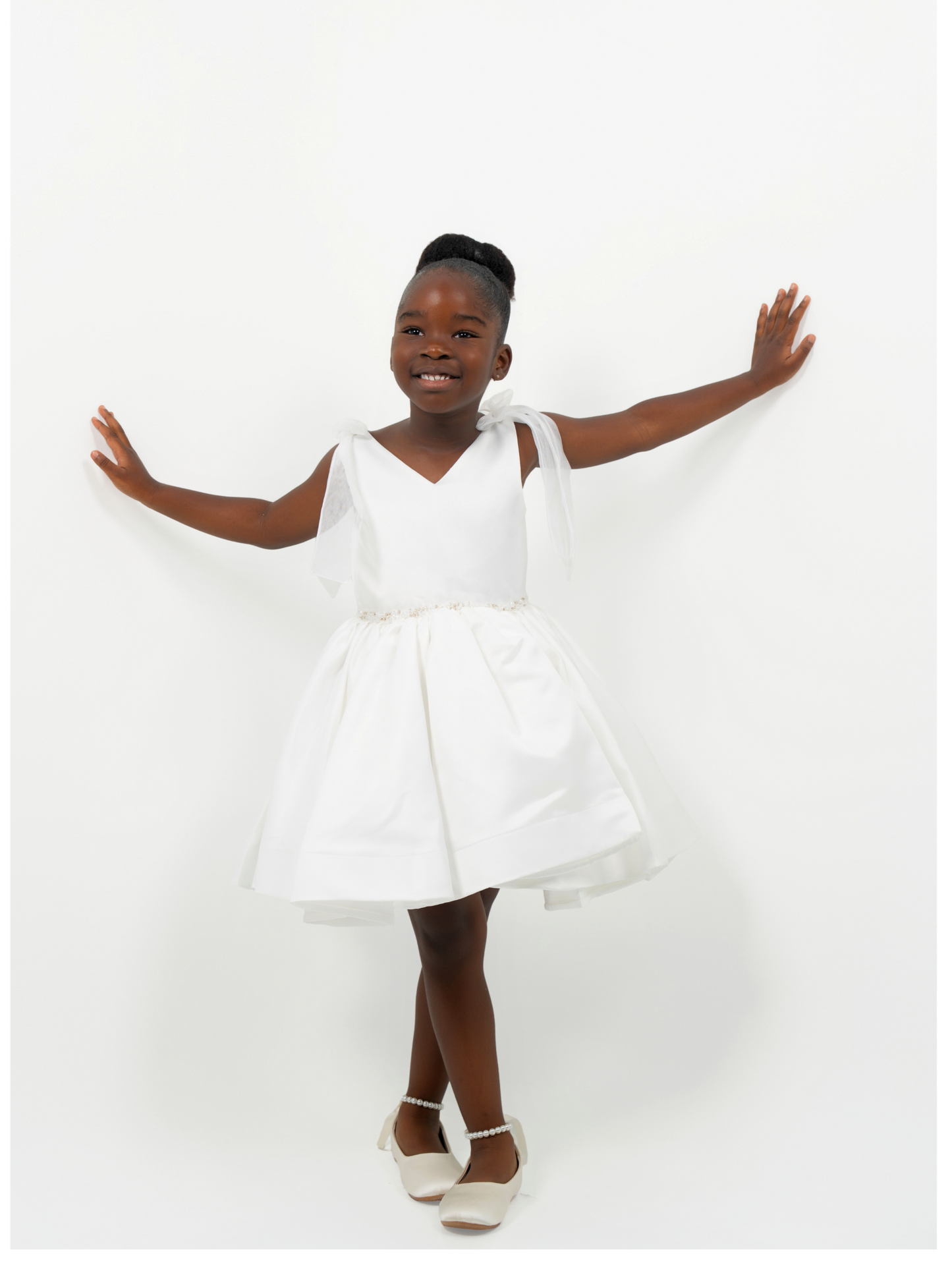 Girl wearing white satin dress with bow straps and full skirt, perfect for flower girl or birthday