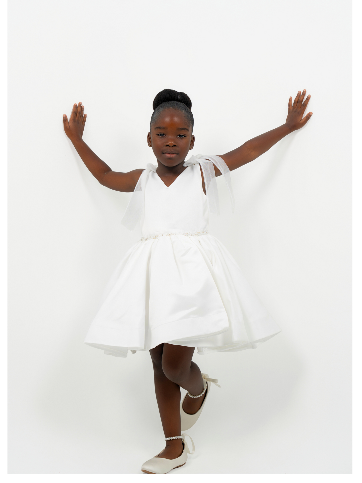 Girl wearing white satin dress with bow straps and full skirt, perfect for flower girl or birthday