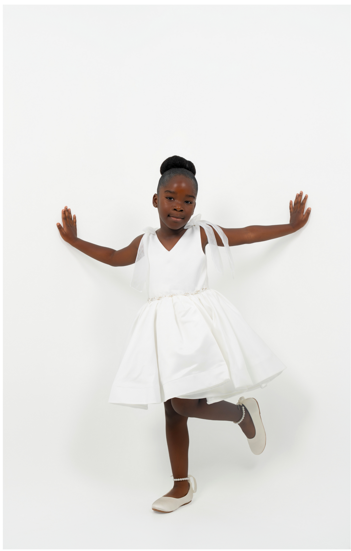 Girl wearing white satin dress with bow straps and full skirt, perfect for flower girl or birthday
