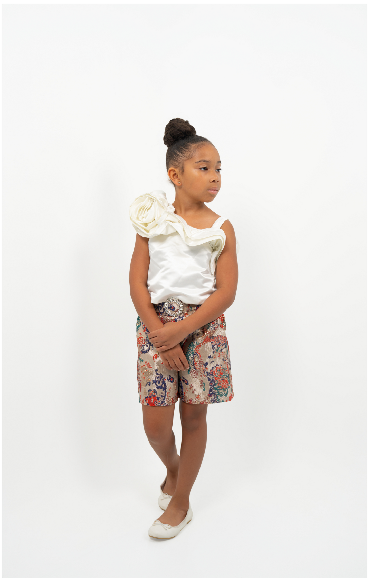Young Girl wearing white satin flower-shoulder top with brocade shorts, styled for elegant party or special occasion