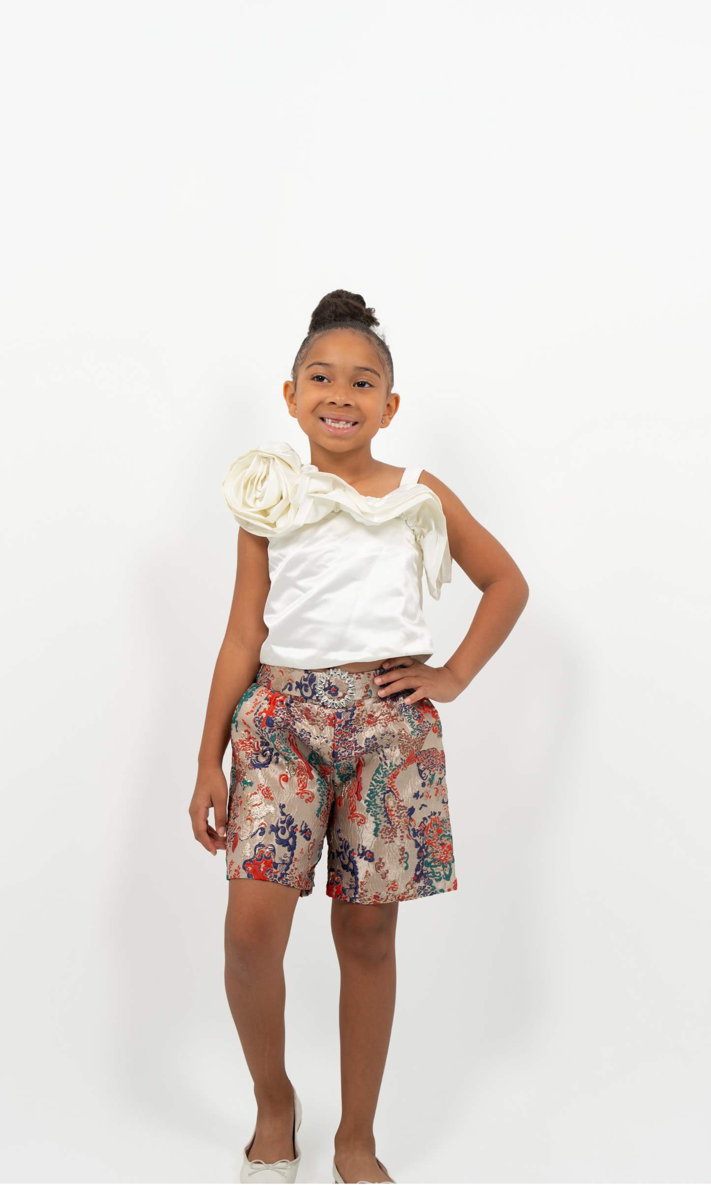 Young Girl wearing white satin flower-shoulder top with brocade shorts, styled for elegant party or special occasion