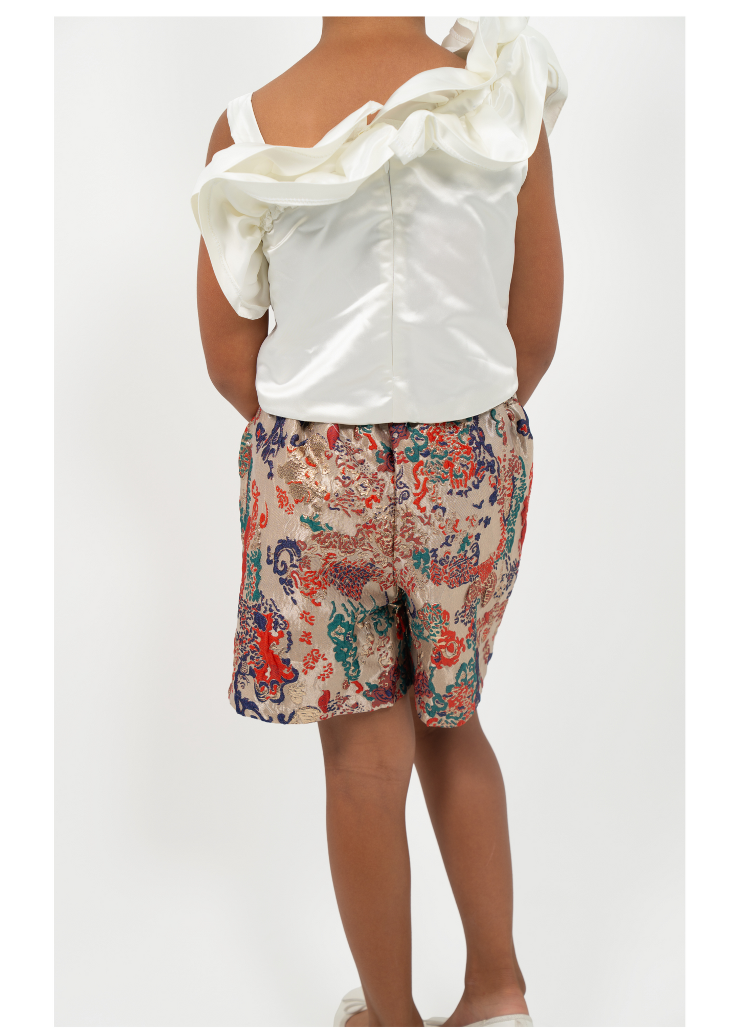 Young Girl wearing white satin flower-shoulder top with brocade shorts, styled for elegant party or special occasion