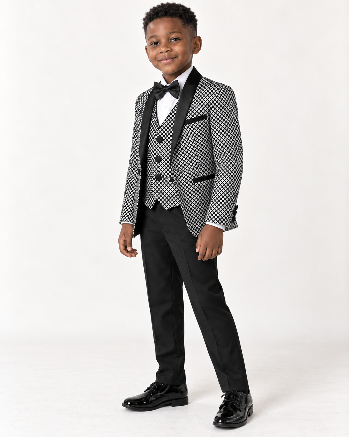 Black boy wearing black and white shimmery five-piece tuxedo, angled view